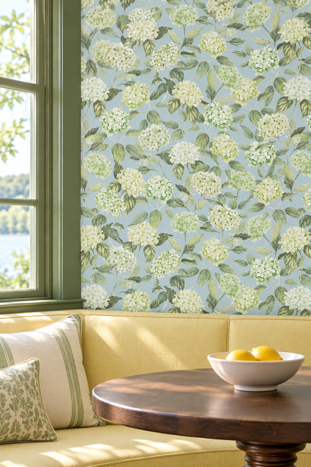 Floral wallpaper with white hydrangea bouquets and green leaves on a light blue background, shown in a styled room setting with a yellow sofa, wooden table, and window.