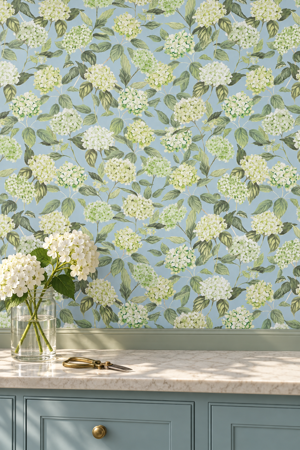 Floral wallpaper featuring white hydrangea blossoms and green leaves on a light blue background, shown installed above a marble countertop with a vase of white flowers and a blue cabinet below.