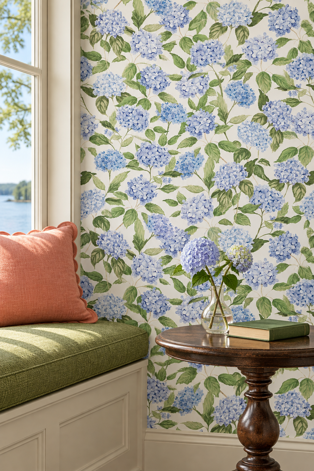 Blue hydrangea floral wallpaper in a beautifully styled room corner featuring a window with a green cushioned bench, a coral pillow, and a small wooden side table.