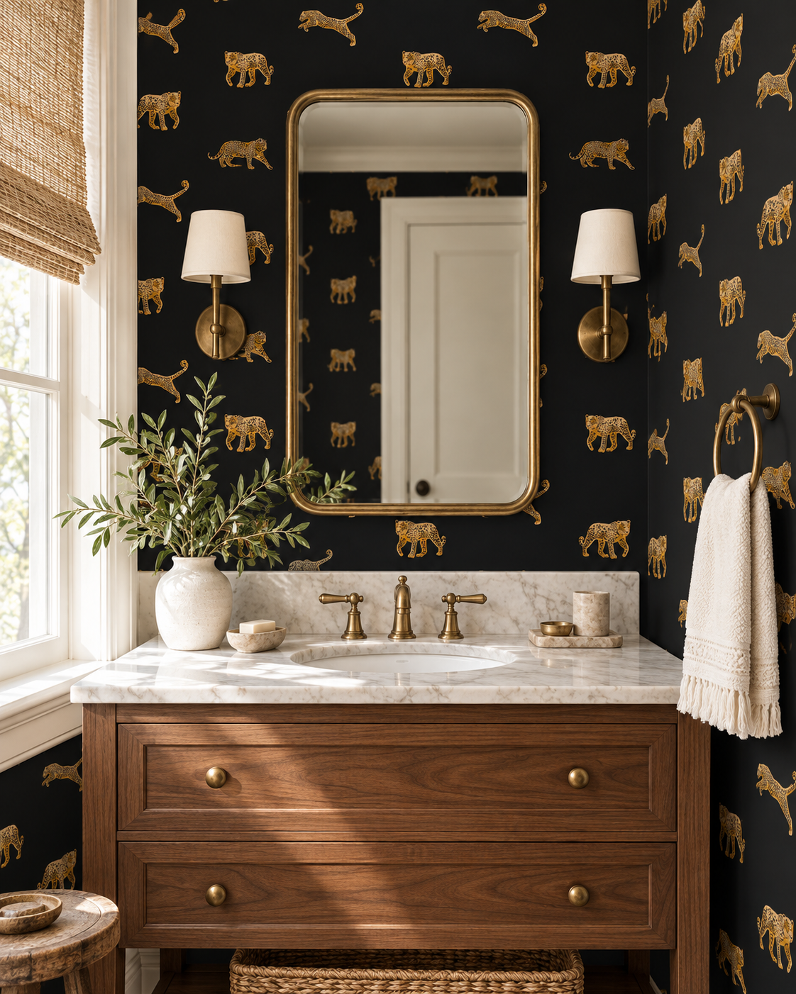 A styled bathroom interior featuring dark wallpaper with a repeating gold animal print, a wooden vanity with a white marble countertop, a large gold-framed mirror, and wall-mounted sconces.