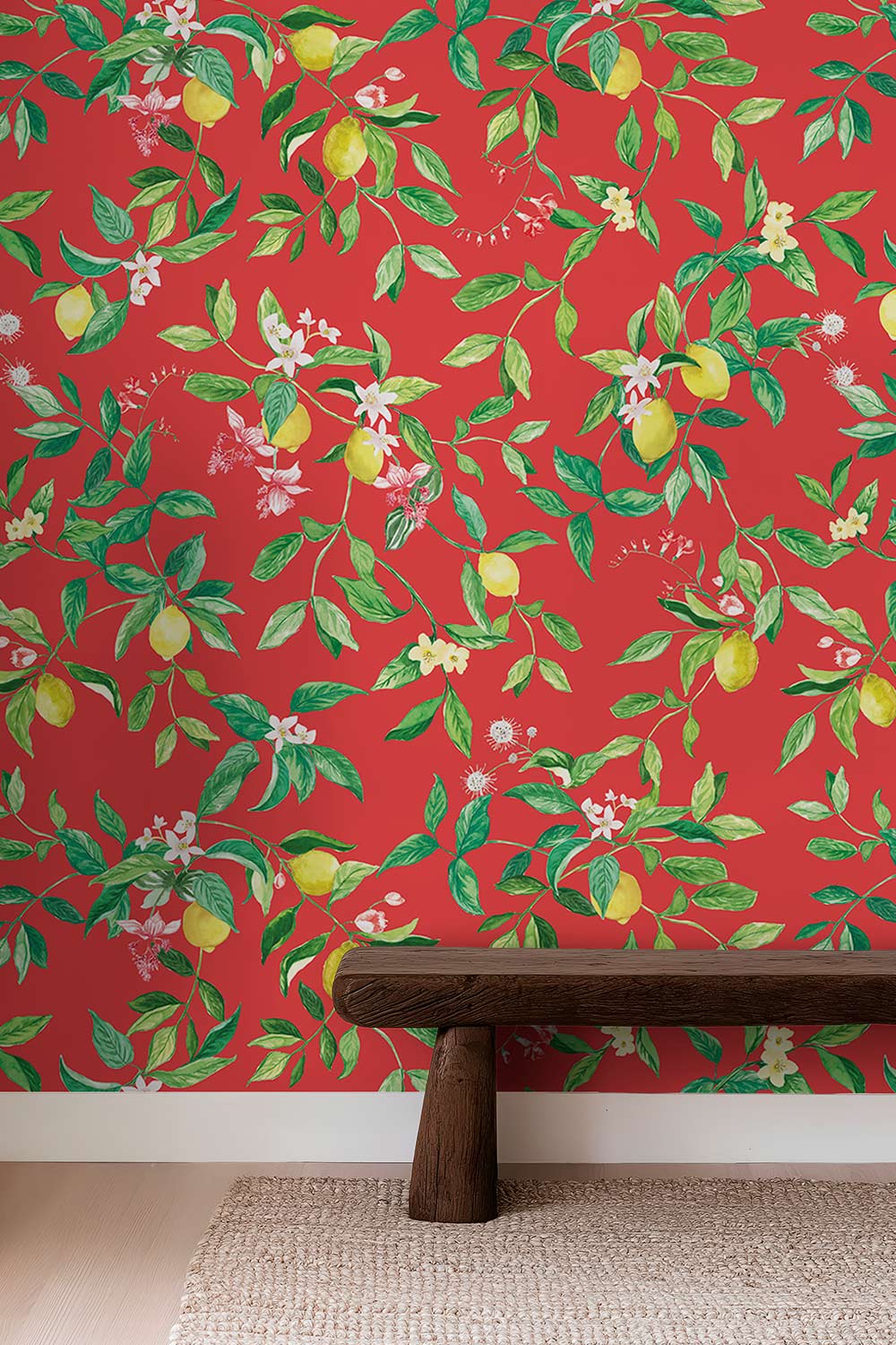 Red wallpaper with a botanical pattern of green leaves, yellow lemons, and small white flowers, shown on a wall above a dark wooden bench and light rug. lemon wallpaper, citrus wallpaper, limoncello wallpaper, white and pastel wallpaper, fruit wallpaper, italian inspired wallpaper, kitchen wallpaper, lemon floral print on all-natural and eco-friendly wall-covering grasscloth and paperweave