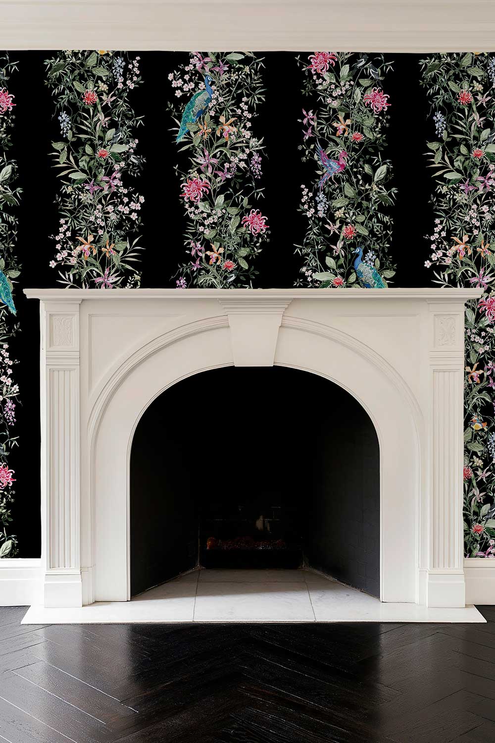 A white fireplace mantel set against black wallpaper with vertical floral and bird motifs, above a dark wood herringbone floor. Hand-painted Mahjong Garden Stripe wallpaper featuring watercolor chinoiserie florals, peacocks, birds, bamboo, and botanical stripes on a rich black background