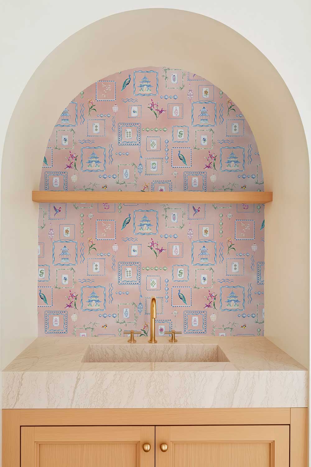 A bathroom vanity area with a pink patterned wallpaper backsplash, a light wood floating shelf, a marble countertop, and a brass faucet. The scene is framed by a beige arched niche. Washable performance vinyl Mahjong Tiles wallpaper with hand-painted chinoiserie details, perfect for powder rooms, bathrooms, game rooms, and clubs.