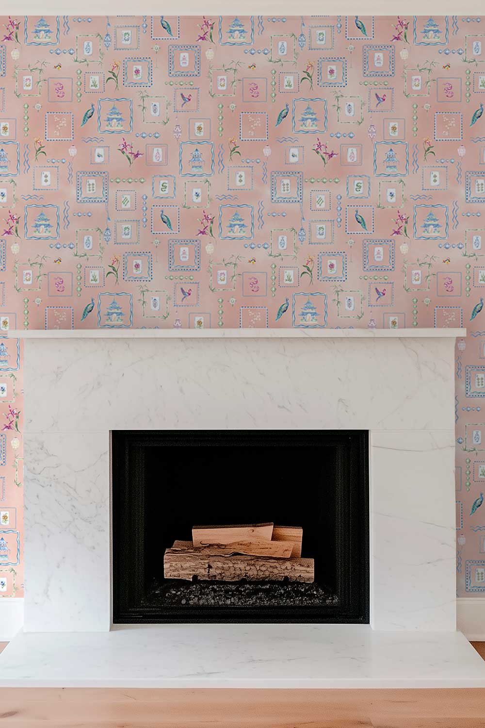A fireplace with a white marble mantel and black firebox insert, set against pink patterned wallpaper featuring small blue and green decorative motifs. Soft pink coral Mahjong Tiles traditional matte wallpaper featuring hand-painted pastel watercolor mahjong tiles, pagodas, bamboo, ginger jars, birds, lanterns, and floral chinoiserie details.