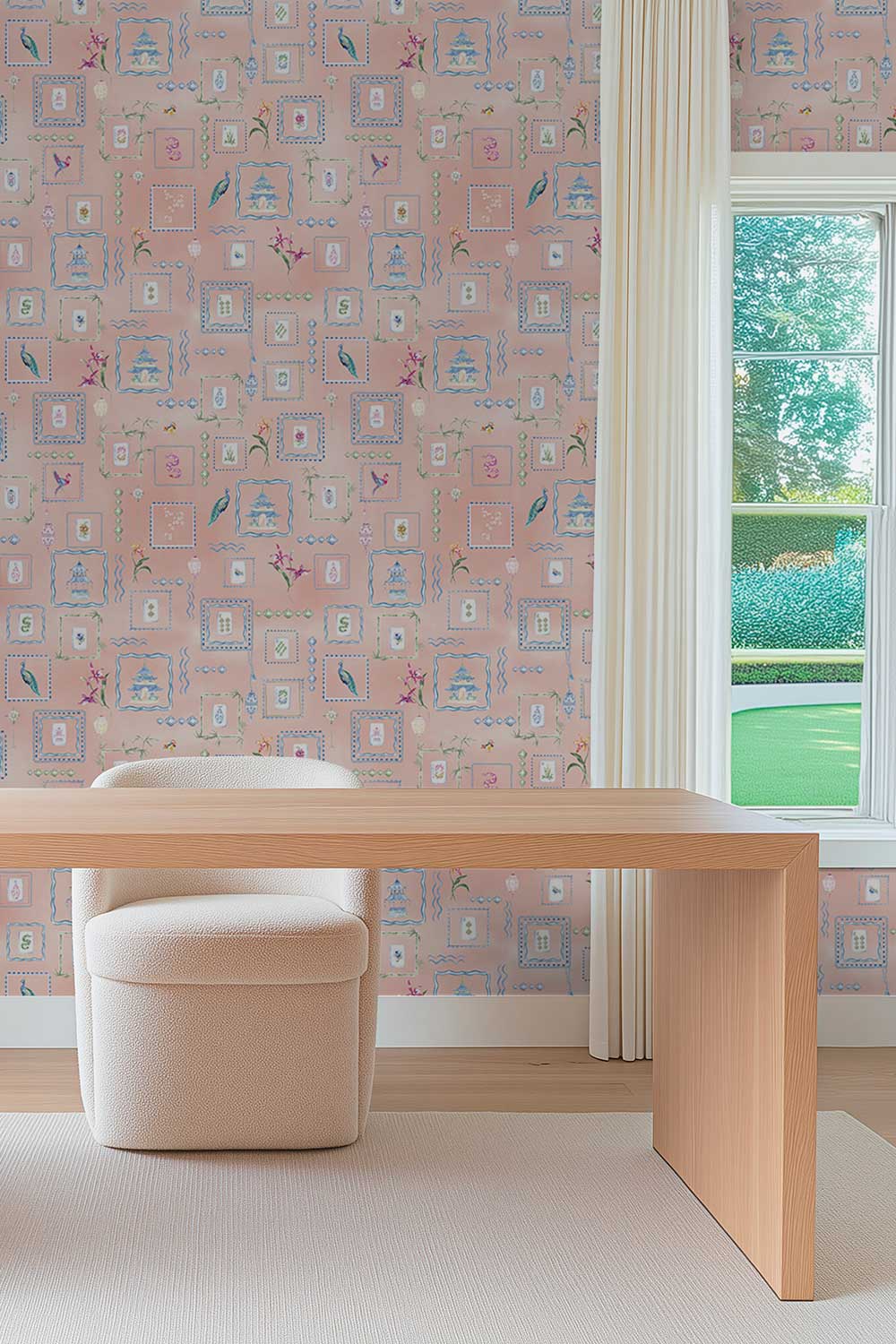 A styled interior room featuring pink patterned wallpaper with a whimsical castle and floral design, a light wood desk, a cream upholstered stool, and a window looking out onto green grass. Soft pink coral Mahjong Tiles traditional matte wallpaper featuring hand-painted pastel watercolor mahjong tiles, pagodas, bamboo, ginger jars, birds, lanterns, and floral chinoiserie details.