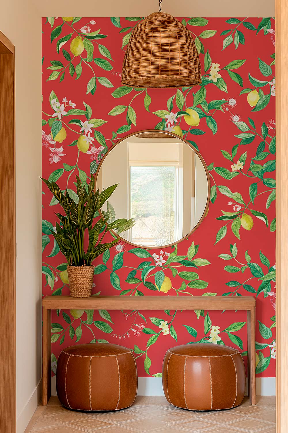 A styled interior corner with a red wallpaper featuring a green botanical and fruit pattern, a round mirror, a wicker pendant light, a wooden console table, a potted plant, and two brown leather poufs. lemon wallpaper, citrus wallpaper, limoncello wallpaper, blue wallpaper, fruit wallpaper, italian inspired wallpaper, kitchen wallpaper, lemon floral print on eco friendly traditional matte luxury wall covering