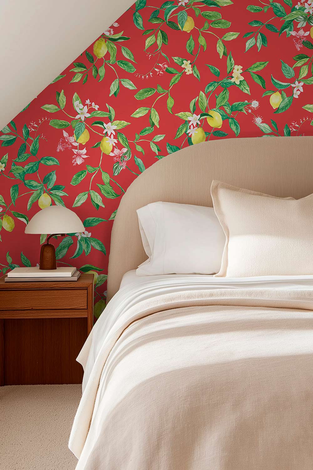 A styled bedroom corner featuring a bed with cream bedding, a wooden bedside table with a lamp, and a bold red wallpaper with green botanical and fruit motifs on the sloped wall. lemon wallpaper, citrus wallpaper, limoncello wallpaper, blue wallpaper, fruit wallpaper, italian inspired wallpaper, kitchen wallpaper, lemon floral print on eco friendly traditional matte luxury wall covering
