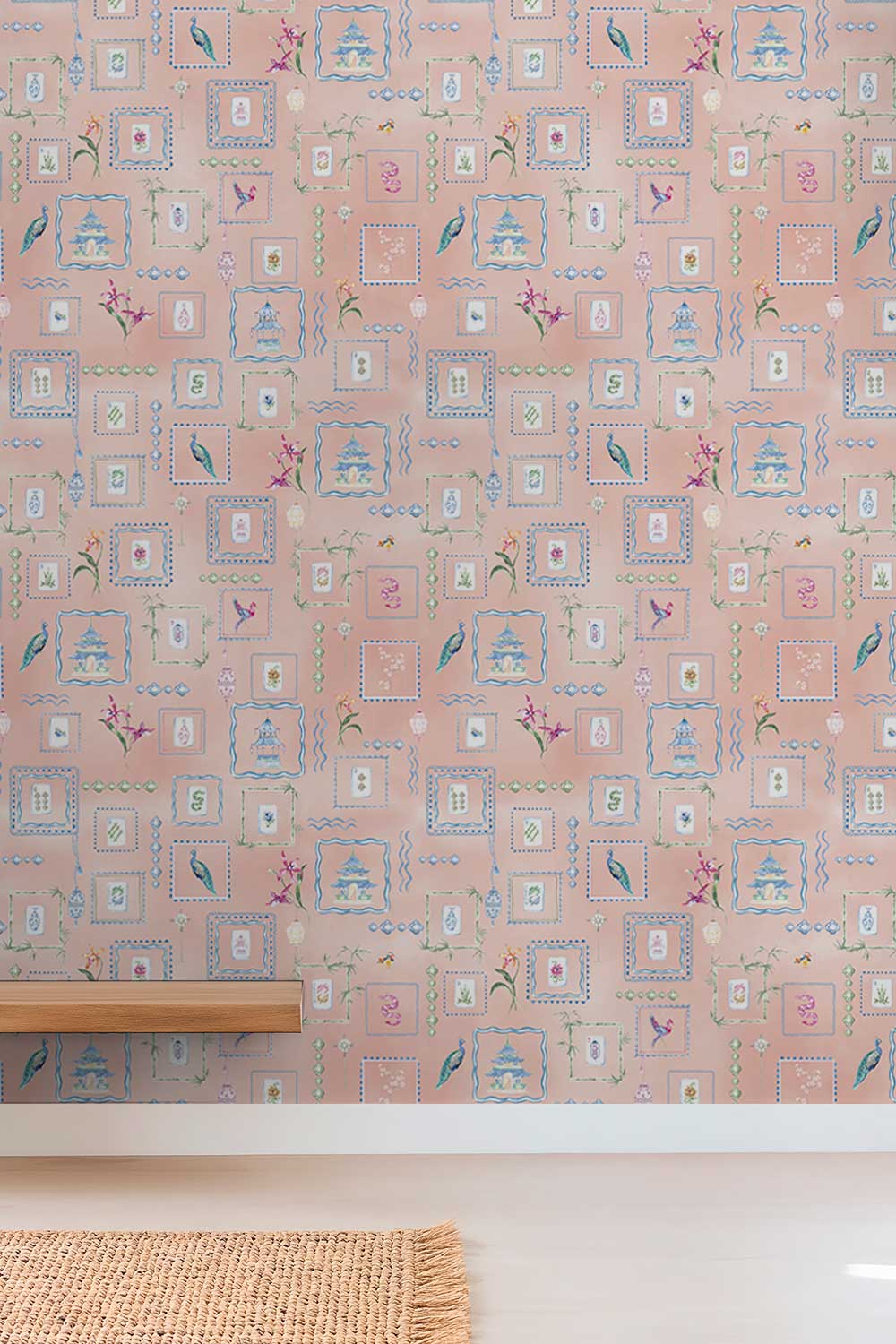 Pink wallpaper with a repeating vintage-style pattern of birdcages, framed motifs, and small floral details, shown on a wall above a light-colored floor with a wooden shelf and woven rug partially visible. Hand-painted watercolor Mahjong Tiles wallpaper featuring mahjong tiles, pagodas, bamboo, birds, ginger jars, lanterns, and chinoiserie artwork on a soft pink coral background printed on an all-natural and eco-friendly grasscloth wall-covering.