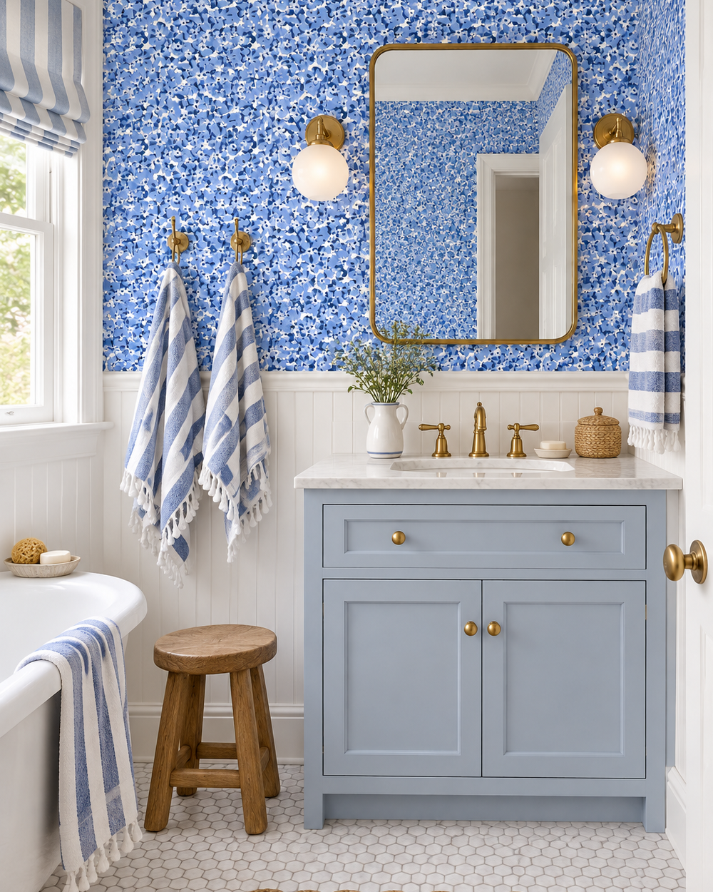 A styled bathroom vanity featuring a light blue cabinet, a white marble countertop, a gold-framed mirror, and a bold blue and white floral wallpaper. Blue and white striped towels hang from brass hooks on the wall, and a wooden stool sits in front of the vanity. vintage inspired garden botanical flower wallpaper in bright blue printed on commercial grade water and stain resistant performance vinyl wall-covering, great for bathrooms, kitchens and commercial spaces.