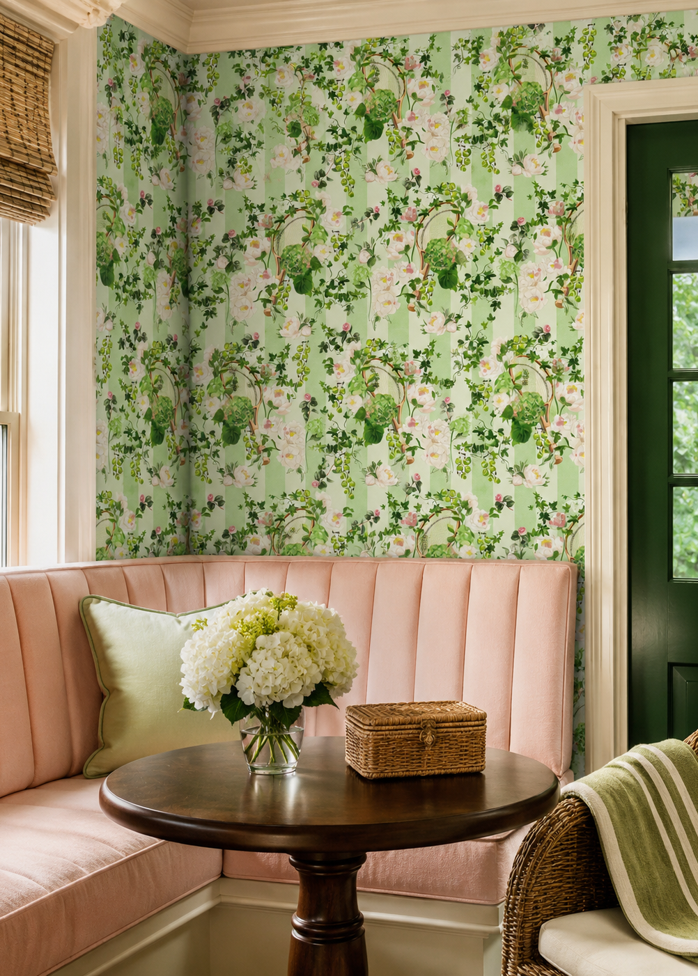 A cozy interior corner with pale pink upholstered bannister seating, wallpapered in a green and pink floral vine pattern, a dark wood table with white flowers, and a green door. Tennis garden party performance wallpaper
performance vinyl wallpaper
tennis club commercial wallcovering
country club vinyl wallpaper
durable botanical stripe wallpaper
hospitality tennis wallpaper
commercial floral wallpaper
cleanable club wallpaper
luxury vinyl wallcovering