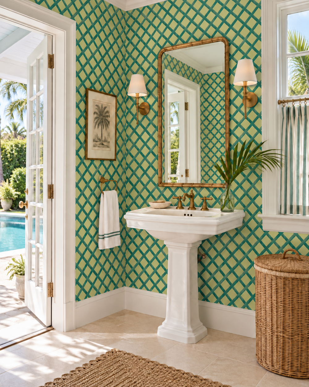 A bright bathroom corner with green geometric pattern wallpaper, a white pedestal sink, a large gold-framed mirror, wall sconces, a framed palm print, and an open door revealing a poolside setting. Tropicana Trellis Boxwood Green geometrical luxury commercial grade washable and stain resistant wallpaper, perfect for bathrooms, kitchens dining rooms and high traffic spaces.